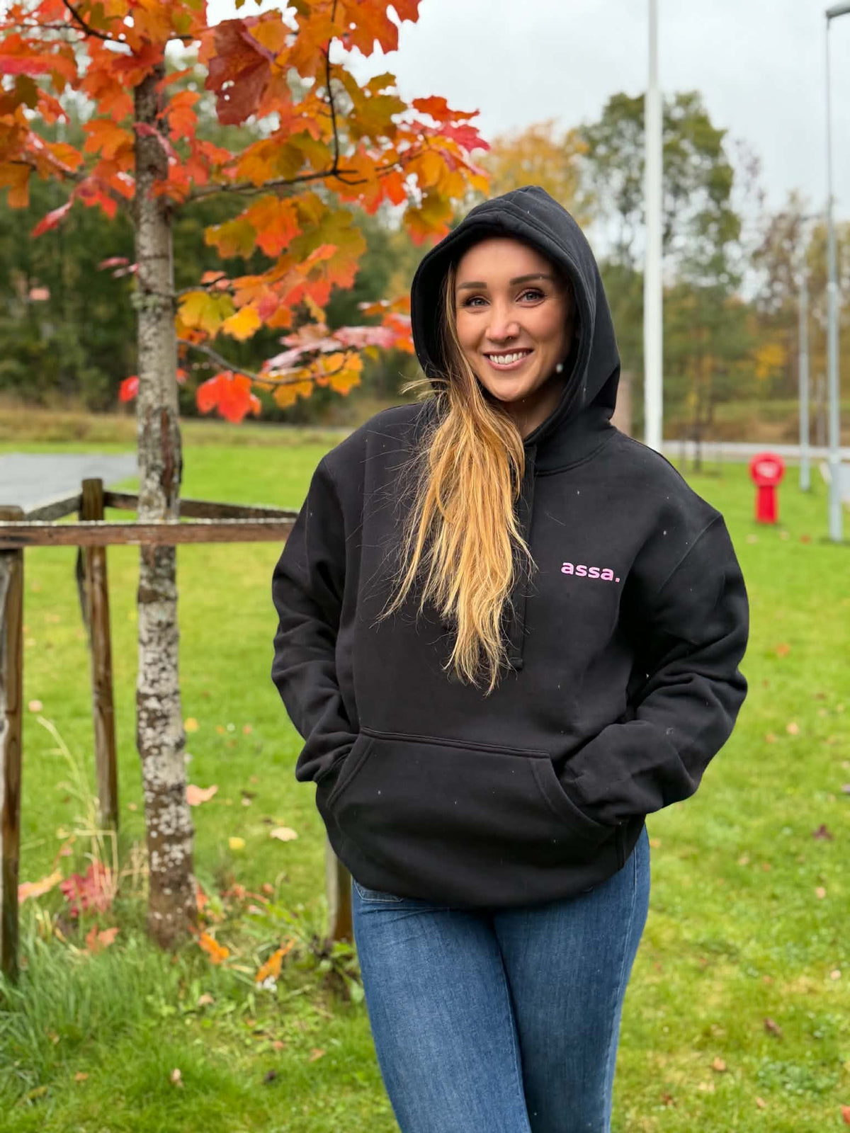 Svart assa.-hoody med rosa glittertrykk og hetten oppe